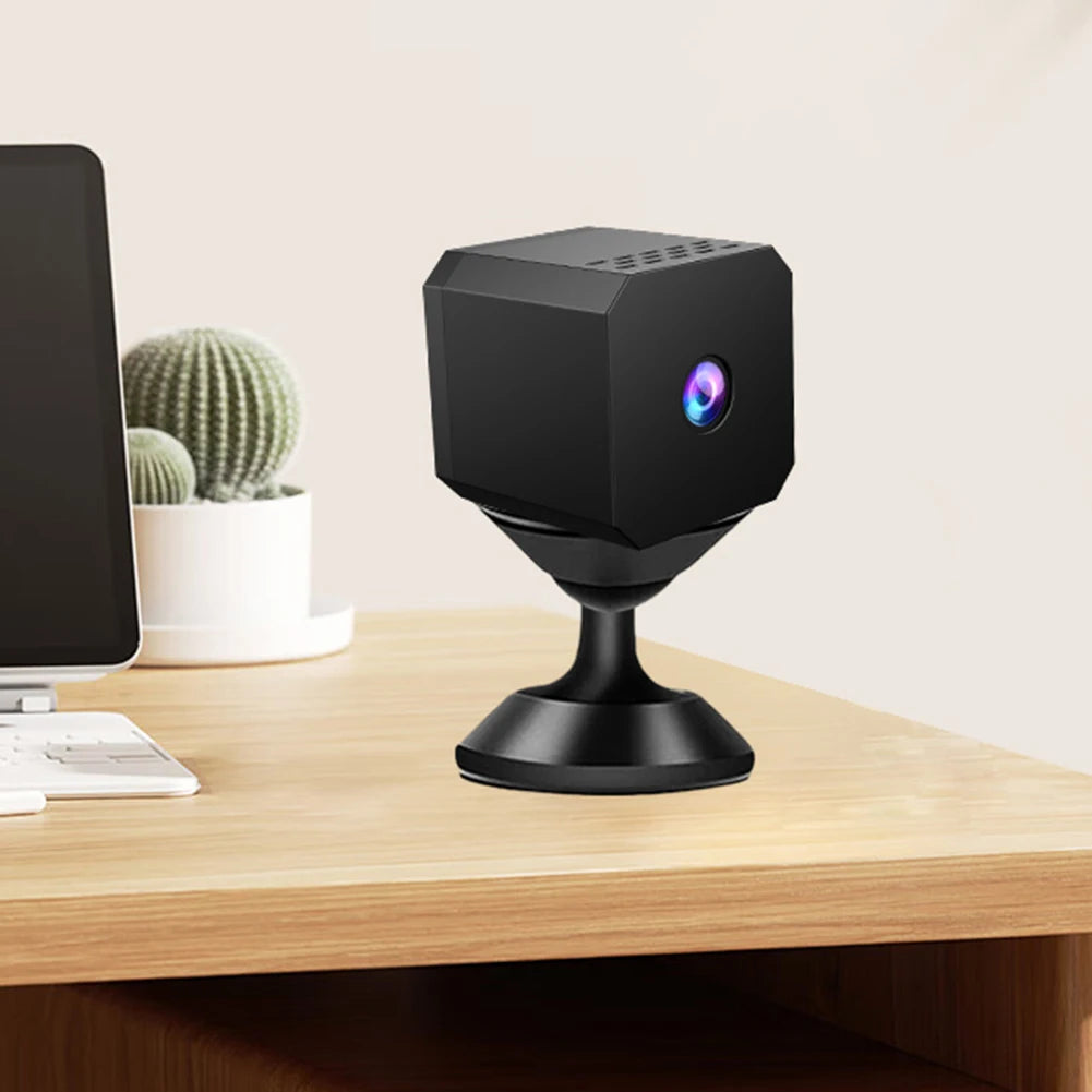 Black hexagonal camera on a wooden desk with a computer monitor and cactus in the background